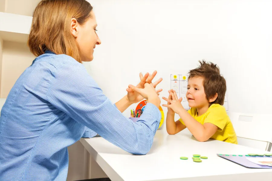 A therapist and a young boy doing a hand exercise at a table