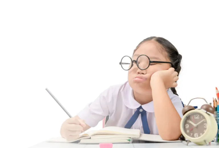 A young girl in glasses resting her chin on her hand while doing homework